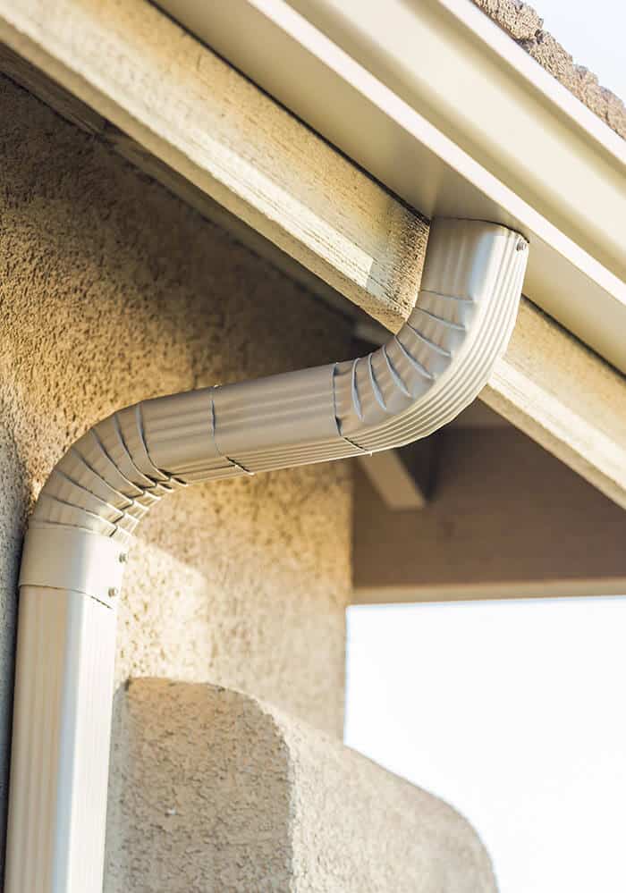 Up close image of a white gutter system connecting to the drain